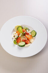 Quick and healthy food recipes. Salad with salmon, vegetables, herbs and capers on white plate. Mediterranean dish recipes. Vertical shot