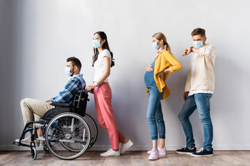 Multiethnic people in medical mask standing near disabled man and pregnant woman in hall