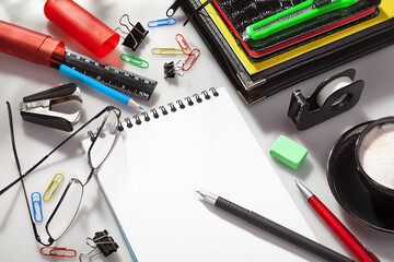 Education,office and workspace concept.Accessories,supplies of secretary, student. Colorful stationery, spectacles and cup of coffee on the desk.Top view of blank white open notebook.Office still life