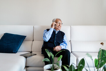 Old man with tie talking on the phone sitting on the couch