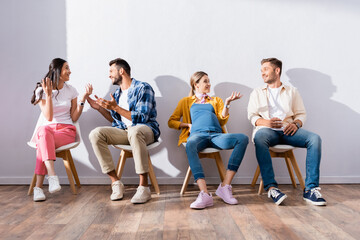 Smiling multiethnic people talking on chairs in hall