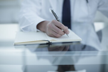 Doctor keeps notes at the workplace in his notebook with a pen in the hospital room