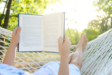 Young woman reading book in comfortable hammock at green garden, closeup