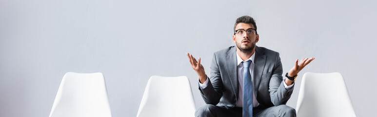 Businessman pointing with hands while waiting on chair in office, banner