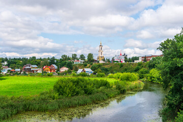 Fototapeta na wymiar View of Suzdal with the Kamenka river, wooden houses and the bell tower of the Rizopoloshensky monastery, Russia.