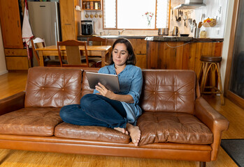 Obraz premium Woman enjoying life at home sitting on sofa using digital tablet. In Coronavirus and New Normal