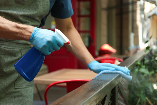 Worker in gloves disinfecting handrail outdoors, closeup