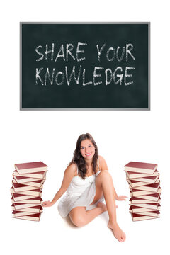 Beautiful Young Woman Sitting Between Two Huge Piles Of Books In Front Of A Blackboard, Share Your Knowledge Is Written On The Board, Isolated On White Studio Background