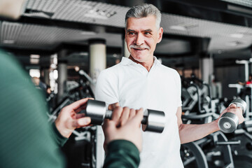 Fototapeta na wymiar Portrait of a mature man performing an exercise with dumbbells, a rehabilitation coach helps him