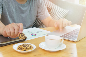 Man working at home with laptop on the table and enjoy with cookies.