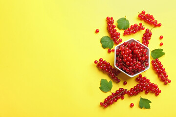 Delicious red currants and leaves on yellow background, flat lay. Space for text