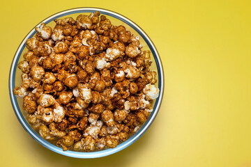 caramel popcorn in a glass bowl on a yellow background, top view