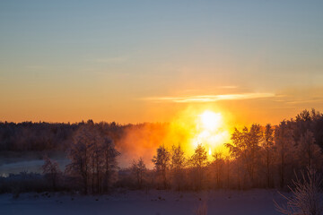 Fabulous winter landscape with fog illuminated by the orange light of the winter sun in frosty weather in the forest