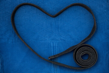 The view from the top. The belt is folded in the form of a heart. Love of judo. Kimono for judo classes and a black belt. The kimono is blue. Background, texture.