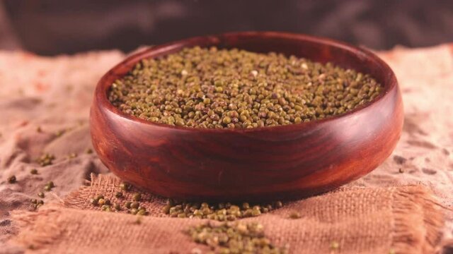 Moong is being picked with a wooden spoon,moong is lying inside a wooden bowl,Green mung beans flso know as mung dal,