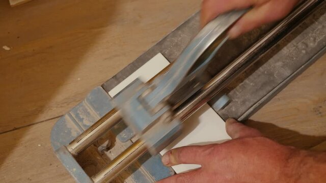 Tiler with a hand-held tile cutter cuts the tile on the floor, person cutting ceramic tiles close up