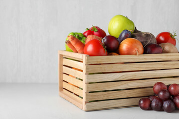 Wooden crate full of different vegetables and fruits on light table. Harvesting time