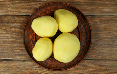 Raw peeled potatoes lie in a ceramic plate.The plate is on a wooden table. Top view