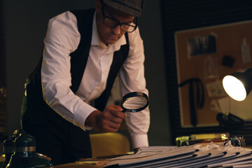 Old fashioned detective with magnifying glass working in office