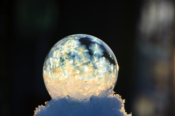 A frozen bubble in the snow with bokeh in the background. Beautiful frosty patterns on a frozen soap bubble. close-up, winter, frosty background. Frozen bubble at sunset light