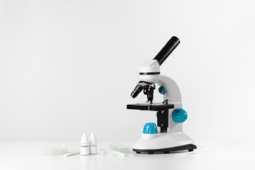 Optical microscope and laboratory supplies on a white table. Chemical research, biology lesson. Copy space for text.