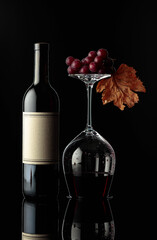 Bottle of red wine and an inverted glass with wine on a black background.