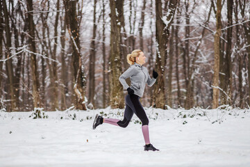 Fototapeta na wymiar Fast slim sportswoman running in forest at snowy winter day. Race, jogging in nature, winter fitness