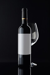 Bottle of red wine and empty glass on a black background.