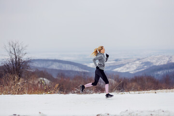 Naklejka na ściany i meble Sportswoman running fast in nature on snowy path at winter. Healthy lifestyle, winter fitness, cold weather