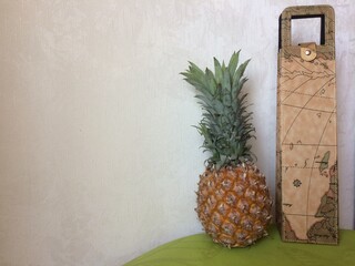 Composition of pineapple and leather pack with geography theme on table with green napkin. Pineapple is tropical fruit that is good for human health.  pale gray background
