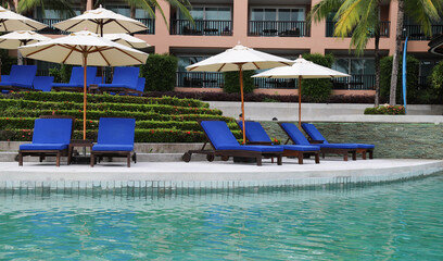 Closeup of blue beach chairs and umbrellas with swimming pool foreground. 