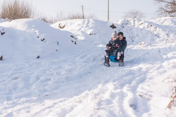 Fototapeta na wymiar Happy dad and little boy playing with snow sled. Father and son sledding during winter holiday.