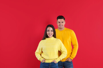 Obraz premium Happy couple wearing yellow warm sweaters on red background
