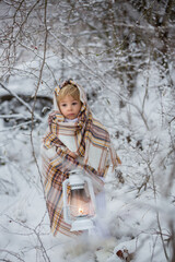 Beautiful blond toddler child, boy with white knitted handmade overall, holding lantern in the snow