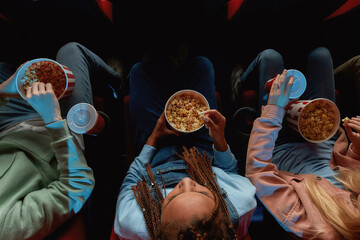 Top view of friends holding baskets of popcorn while watching movie together at the cinema