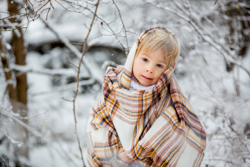 Beautiful blond toddler child, boy with white knitted handmade overall, holding lantern in the snow
