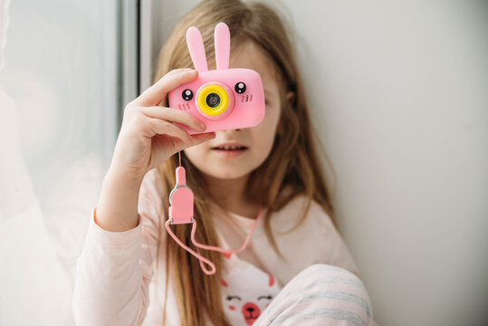 Little beautiful girl makes a selfie on a pink camera.