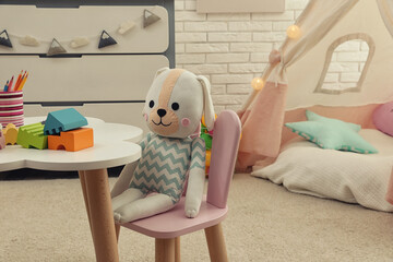 Cute toy bunny on small chair in playroom. Interior design