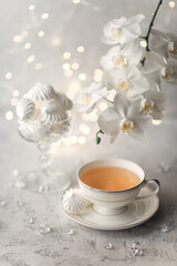 Cozy home spring breakfast still life. A porcelain cup of hot green tea with a marshmallow dessert on a gray background is decorated with a flowering branch of a white otchid. Spring concept. 