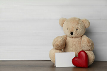 Cute teddy bear with heart and blank card on wooden table, space for text. Valentine's day celebration