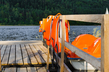 Orange catamarans on lake moored at the pier. Pleasure boats with life jackets.