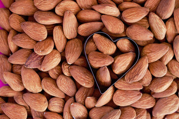 Almonds heap in heart shape on pink background. Isolated. Valentine's Day. Flat lay. Top view. Raw food.