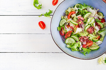 Ketogenic salad with prosciutto, tomatoes, cucumber, lettuce, red onion  and cheese  in  bowl.  Concept healthy appetizer. Keto, paleo food. Top view, overhead, copy space