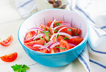Fresh tomatoes with red onion and spices in a blue bowl.  Concept healthy appetizer. White wooden background.