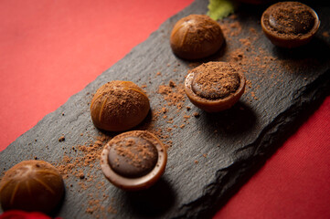 Chocolates lie on a slate on a red table surface. Festive table setting. Dessert serving. Romance. A romantic dessert for the holiday. Sweet gift.