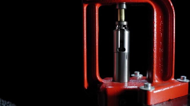 The process of making a rifle cartridge. Hand press and ammo shell against dark background, soft focus. Copy space