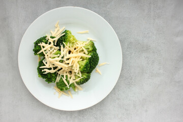 Broccoli with grated cheese on a plate on gray concrete background. Healthy food. Flat lay, close-up