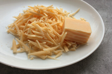 Grated cheese and a piece of cheese on a plate. Overhead view. Close-up