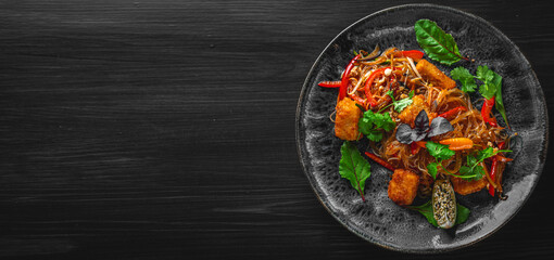Tasty asian noodles with fried cheese tofu and vegetables in plate on black wooden table background