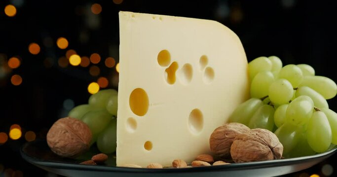 Close up part of Medium hard cheese head edam gouda parmesan on wooden board, with nuts and grapes rotaiting on the plate.